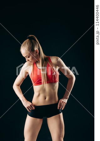 Muscular slender stylish girl standing looking down with her hands on hips Muscular slender stylish girl standing looking down with her hands on hips 114400446