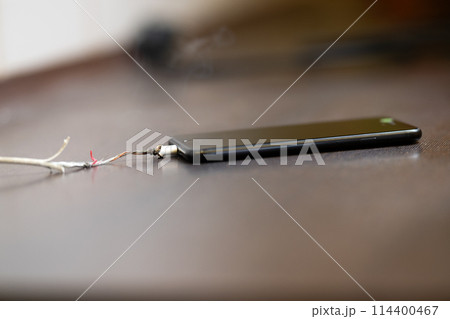 The smartphone is charging from a faulty cable. The concept of danger, the use of non-standard equipment, worn-out equipment The smartphone is charging from a faulty cable. The concept of danger, the use of non-standard equipment, worn-out equipment 114400467