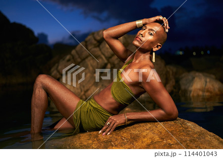 Gender fluid black person poses in creek laying on rocks in natural water pool. Queer ethnic fashion model in revealing clothes wears brass earrings, golden nose-ring, rings, bracelets lying in lake. Gender fluid black person poses in creek laying on rocks in natural water pool. Queer ethnic fashion model in revealing clothes wears brass earrings, golden nose-ring, rings, bracelets lying in lake. 114401043