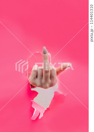 Woman hand showing middle finger through a ripped hole in pink paper 114401310
