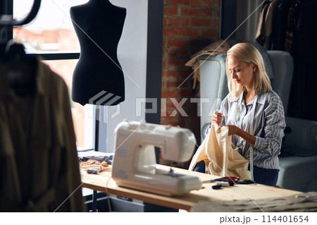 young blonde dressmaker repairing client's clothes young blonde dressmaker repairing client's clothes 114401654