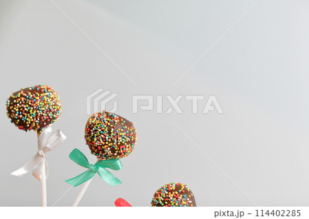 Cake Pops in chocolate with colored sprinkles. Decorated with a ribbon bow. On a white background. 114402285