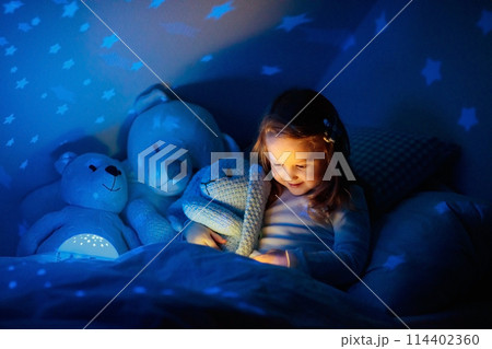 Little girl reading a book in bed 114402360