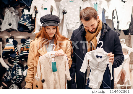 attractive caucasian woman holding baby's wear and man next to her attractive caucasian woman holding baby's wear and man next to her 114402861