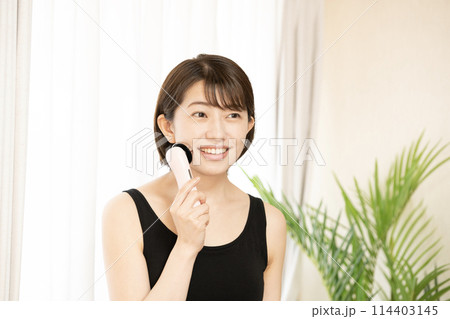 美顔器を頬にあてて微笑む女性 114403145