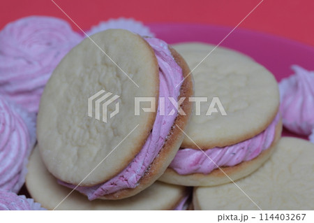 Cooked marshmallow sandwiches. They lie on plate. Next on the plate is a marshmallow of various sizes. 114403267