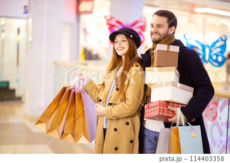 beautiful caucasian couple after shopping holding gifts in mall 114403358