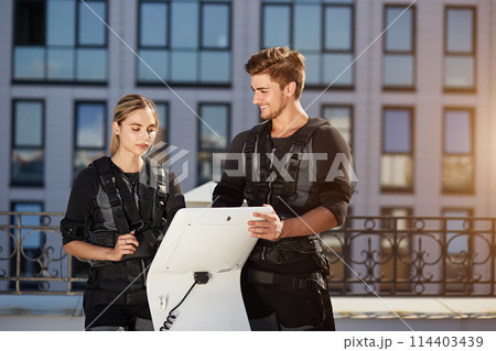 positive male coach showing the working of EMS device to a fit pretty girl 114403439