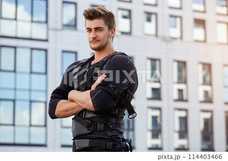 muscular athlete wearing EMS suit is standing on the roof of the building muscular athlete wearing EMS suit is standing on the roof of the building 114403466