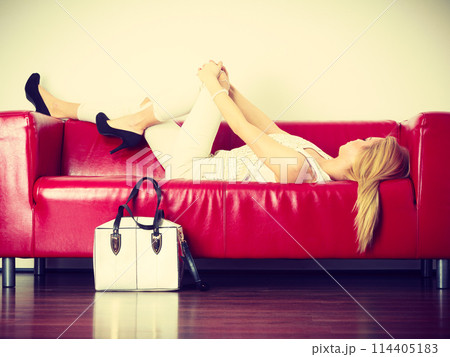 Woman lying on sofa presenting white bag Woman lying on sofa presenting white bag 114405183