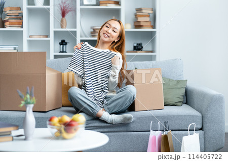 Happy Young Woman Unpacking Clothes In New Home Living Room Happy Young Woman Unpacking Clothes In New Home Living Room 114405722