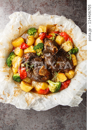 Lamb baked with vegetables and herbs in parchment close-up in a frying pan. Vertical top view Lamb baked with vegetables and herbs in parchment close-up in a frying pan. Vertical top view 114406705