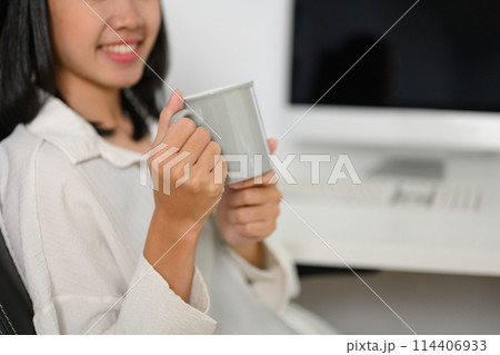Smiling young businesswoman drinking coffee at the desk in the office 114406933