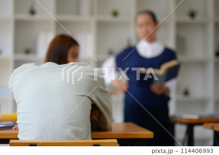 Exhausted young college student man sleeping in classroom between other classmates Exhausted young college student man sleeping in classroom between other classmates 114406993
