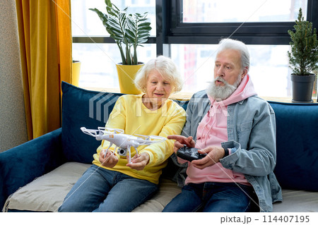 Happy mature couple launch a drone at home, man holding console in hands. Loving spouses Happy mature couple launch a drone at home, man holding console in hands. Loving spouses 114407195
