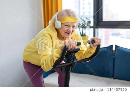 aged woman in mid 70's exercise on stationary bike at home. Active mature female aged woman in mid 70's exercise on stationary bike at home. Active mature female 114407530