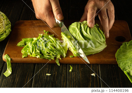 The chef cuts young fresh cabbage with a knife to prepare a salad. Low key concept of preparing a vegetarian dish or healthy food for breakfast The chef cuts young fresh cabbage with a knife to prepare a salad. Low key concept of preparing a vegetarian dish or healthy food for breakfast 114408196