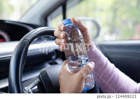 Asian woman driver holding bottle for drink water while driving a car. Plastic hot water bottle cause fire. Asian woman driver holding bottle for drink water while driving a car. Plastic hot water bottle cause fire. 114409221