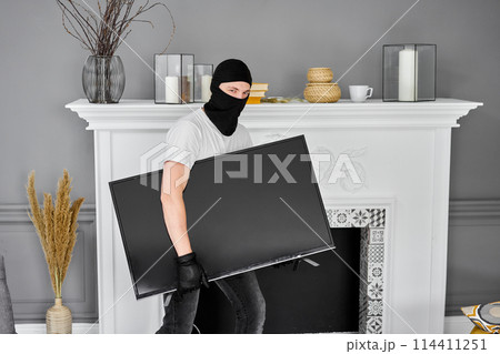 Thief with black balaclava stealing modern expensive television. Masked face. Man burglar stealing tv set from house 114411251