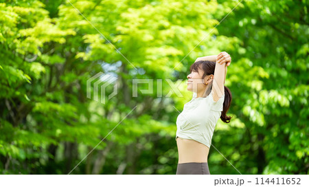 緑の中でストレッチをする笑顔の女性 114411652