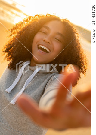 Female Woman Teenage Girl Smiling and Reaching to Camera on a Beach at Sunset 114411720