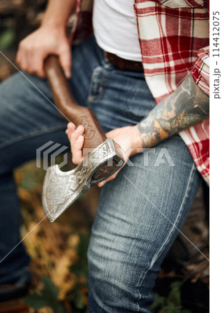 close up man in checkered shirt sitting on logs and holding axe 114412075