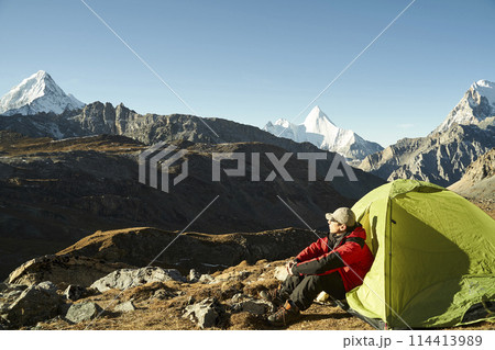 asian man sitting in tent enjoying early morning sunlight in yading national park, china asian man sitting in tent enjoying early morning sunlight in yading national park, china 114413989