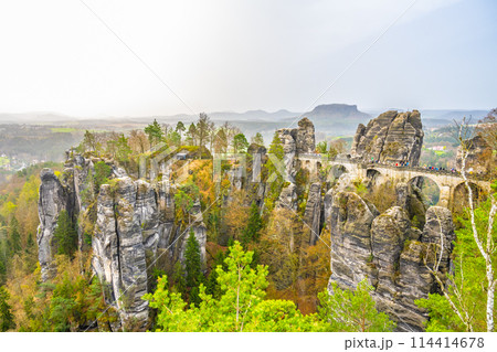 The Bastei Bridge stands tall among majestic sandstone rock formations with visitors enjoying the scenic view at sunset. Kurort Rathen, Saxon Switzerland, Germany The Bastei Bridge stands tall among majestic sandstone rock formations with visitors enjoying the scenic view at sunset. Kurort Rathen, Saxon Switzerland, Germany 114414678
