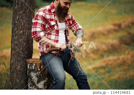 bearded man wipes clean axe with leaves. Bearded axeman. bearded man wipes clean axe with leaves. Bearded axeman. 114414681