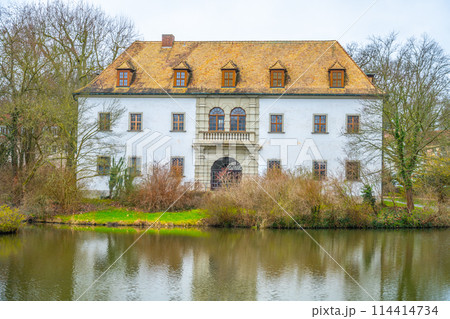 The historic Bad Muskau Chateau stands serene by a calm pond in Saxony, Germany, reflecting its grandeur in the water. 114414734
