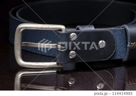 Leather belt with a metal buckle close-up on a dark background. 114414985
