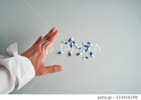 Hand reaches out to a white and blue pill on a blue background. 114416299