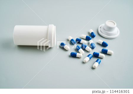Blue and white capsules spilled out of a medicine jar on a blue background. 114416301