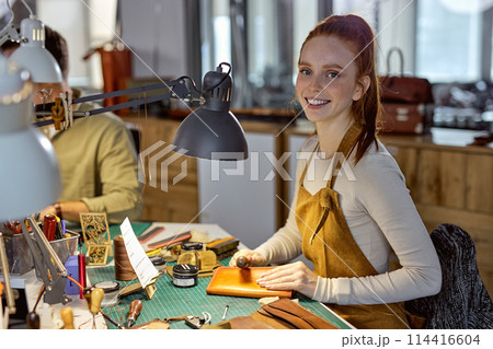 smiling active craftswoman burnishes leather surface smiling active craftswoman burnishes leather surface 114416604
