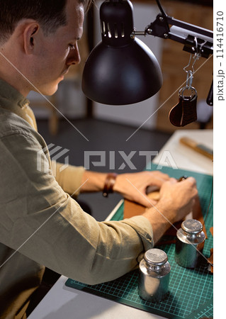 young artisan punctures holes into leather 114416710