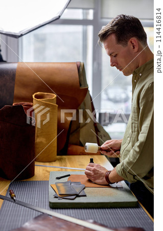 young craftsman making holes along a leather edge 114416814