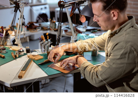 young talented craftsman punctures or enlarges existing holes in leather 114416828