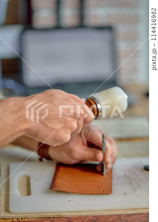 craftsman working with leather stitching punch 114416982