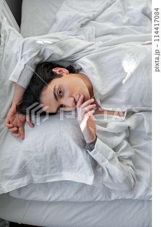 lazy man with hand over forehead is alone at bed and look up at camera lazy man with hand over forehead is alone at bed and look up at camera 114417084