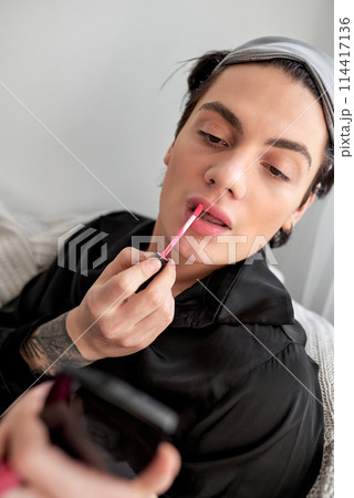 glamorous male in black bathrobe applying pink lipstick on lips 114417136