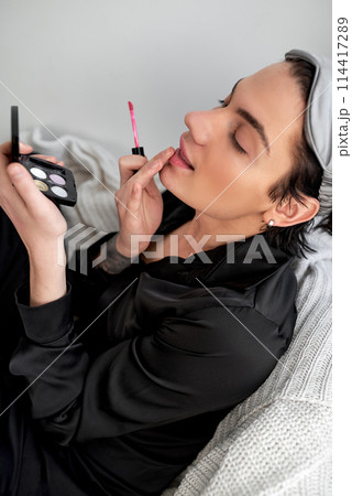 brunette man in an elegant black robe gets pleasure from using cosmetics 114417289