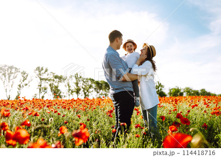 Family with a child walking on a poppy field. Mother, father, little daughter having fun on the poppy field. Family with a child walking on a poppy field. Mother, father, little daughter having fun on the poppy field. 114418716