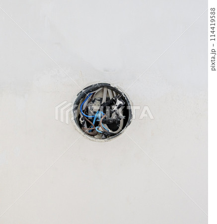 An electrical junction box on a white wall. The electrical wires start from the wall. The concept of laying an electrical cable. An electrical junction box on a white wall. The electrical wires start from the wall. The concept of laying an electrical cable. 114419588