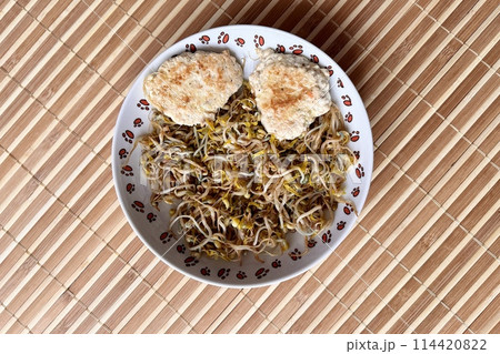 Micro-greenery. Green white sprouted mung beans with two fried cutlet cooking in steam in white plate on the table in bamboo background. Healthy food for people. Close-up Micro-greenery. Green white sprouted mung beans with two fried cutlet cooking in steam in white plate on the table in bamboo background. Healthy food for people. Close-up 114420822