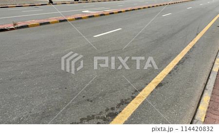 An empty curving auto road with distinct yellow restriction lines, white lane markings and a sidewalk edge 114420832