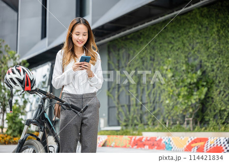 A young businesswoman smiling and holding her smartphone enjoys a bike ride through the city. Her ability to blend work and fun is a testament to the modern concept of work-life balance. A young businesswoman smiling and holding her smartphone enjoys a bike ride through the city. Her ability to blend work and fun is a testament to the modern concept of work-life balance. 114421834