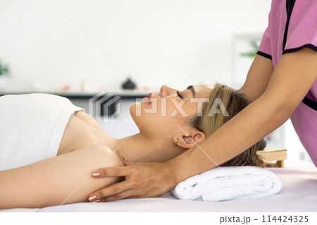 Beautiful asian woman getting body massage in beauty spa. Young woman with closed eyes relaxing in indoor spa while getting shoulder massage. Serene woman relaxing  in a beauty center. Side view 114424325