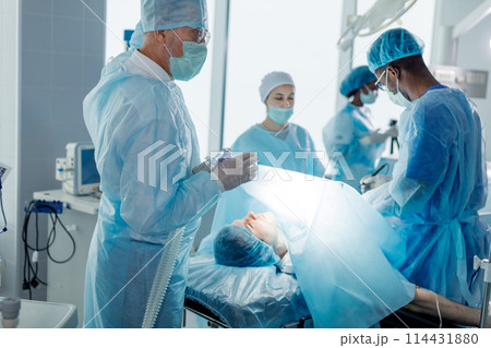 male patient lying on an operating table with surgeons in a surgery room 114431880