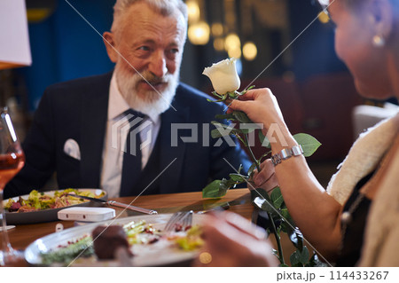 Loving man presenting white flower to his woman. Couple celebrating anniversary in restaurant 114433267