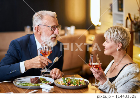 Stylish senior couple taking meal in restaurant, using electronic cigarette. IQOS Stylish senior couple taking meal in restaurant, using electronic cigarette. IQOS 114433328